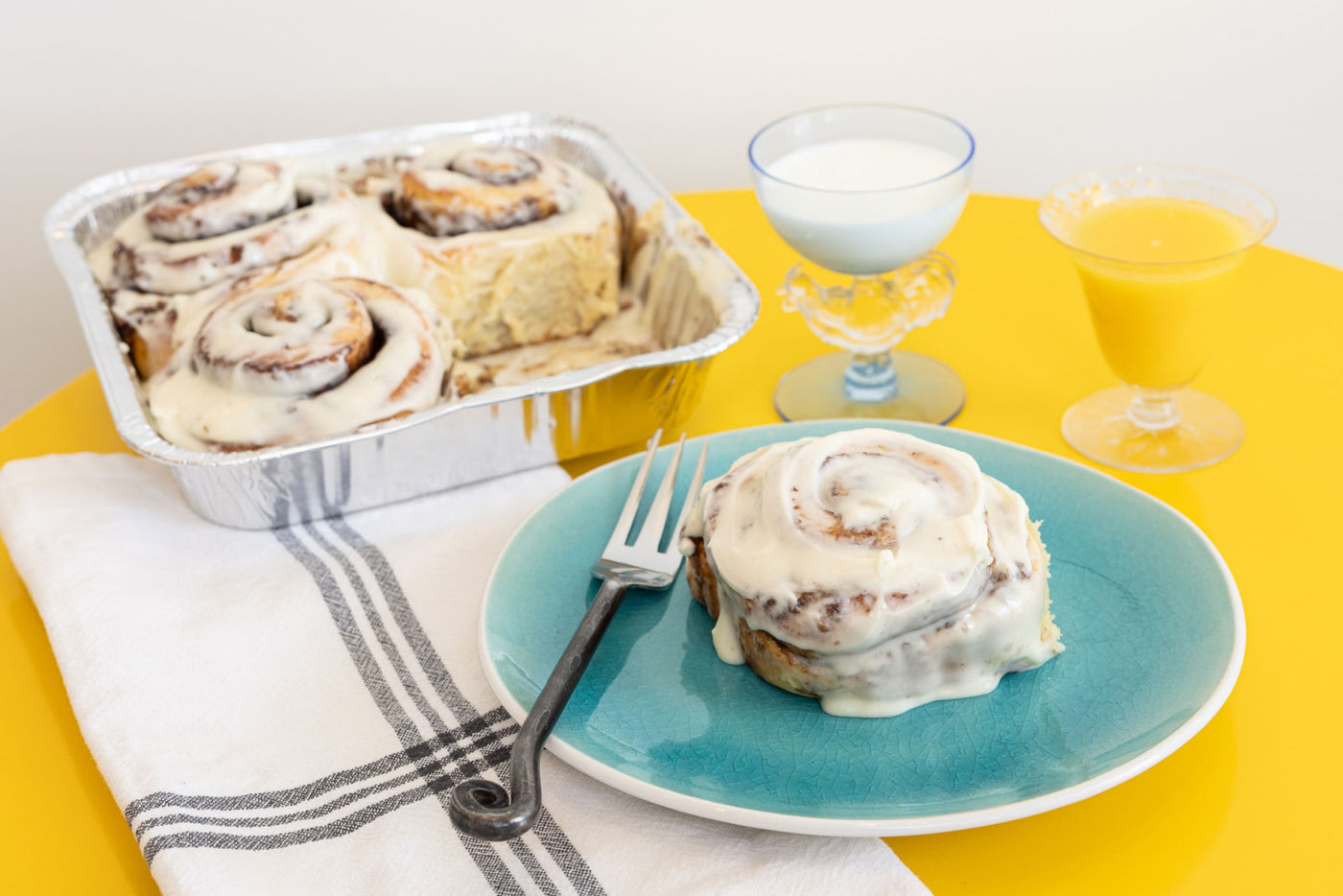 breakfast place setting with tray of frosted cinnamon rolls and glass of OJ and milk