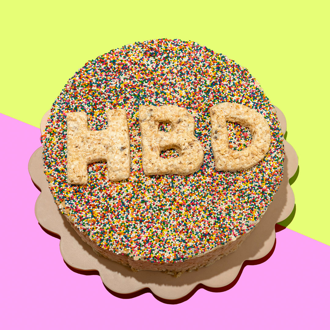 round rice cereal treat cake topped with rainbow sprinkles, with HBD letters on the cake