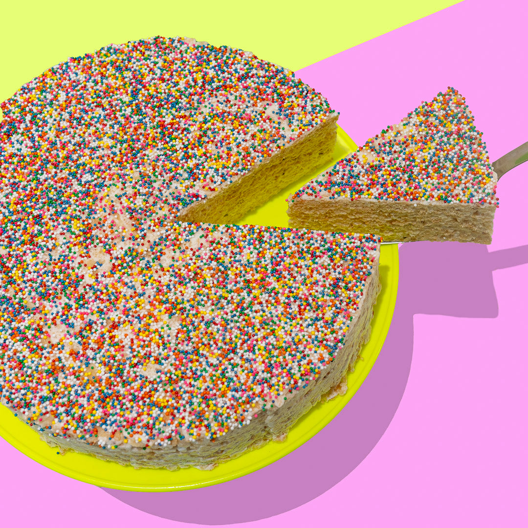 round rice cereal treat cake topped with rainbow sprinkles, with a slice being pulled out of the cake