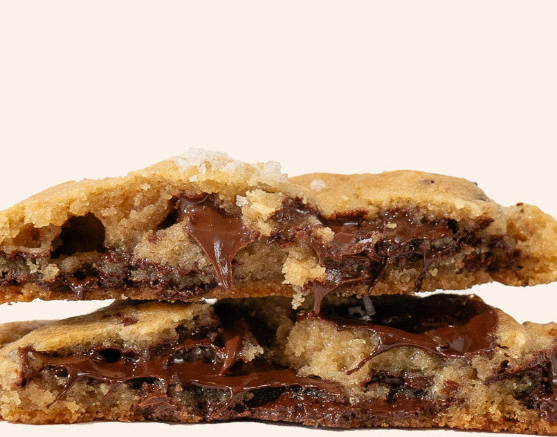 Chocolate chip cookie cut in half to reveal gooey chocolate filling on a white background