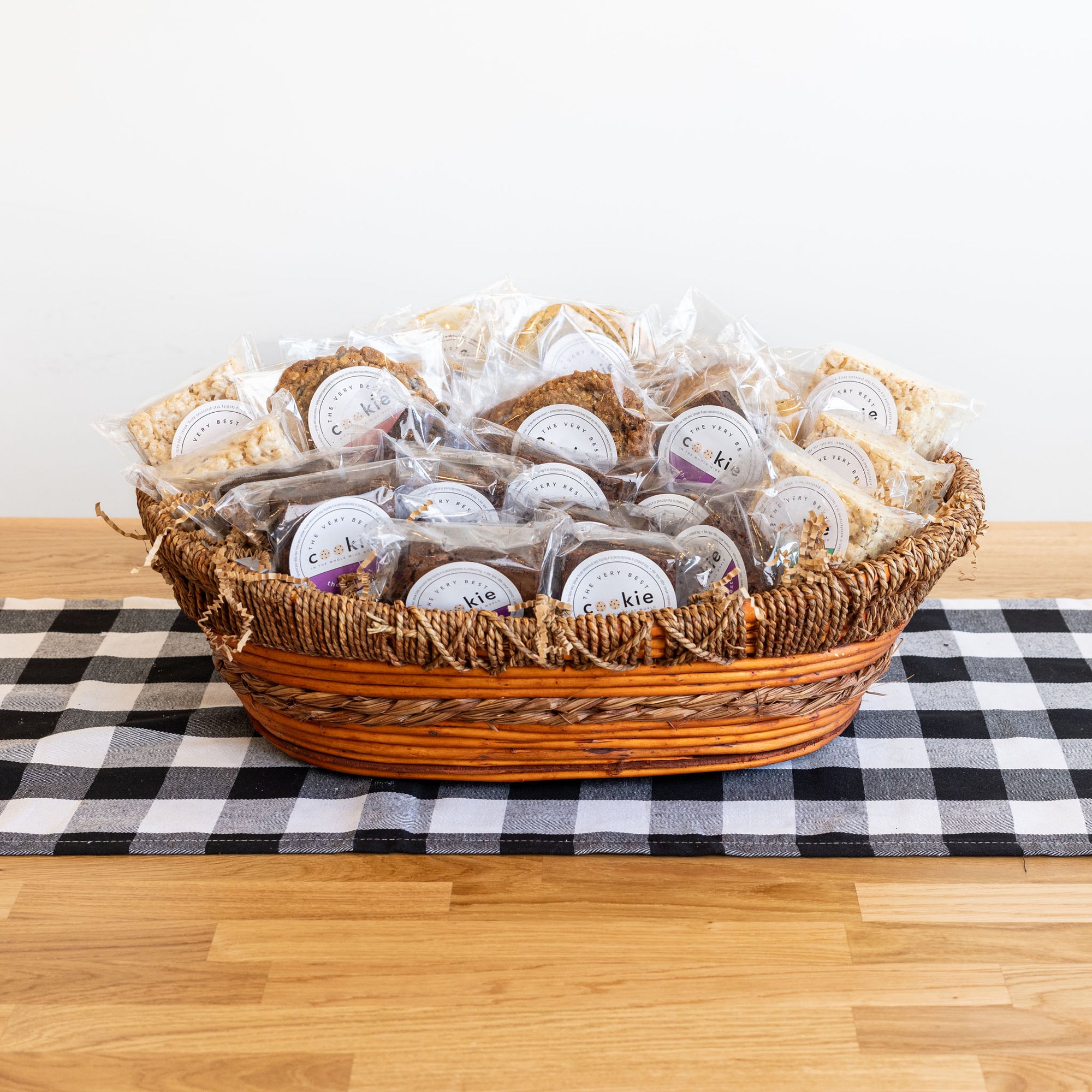 basket full  of wrapped and stickered cookies sitting on a wood table with a checkered runner