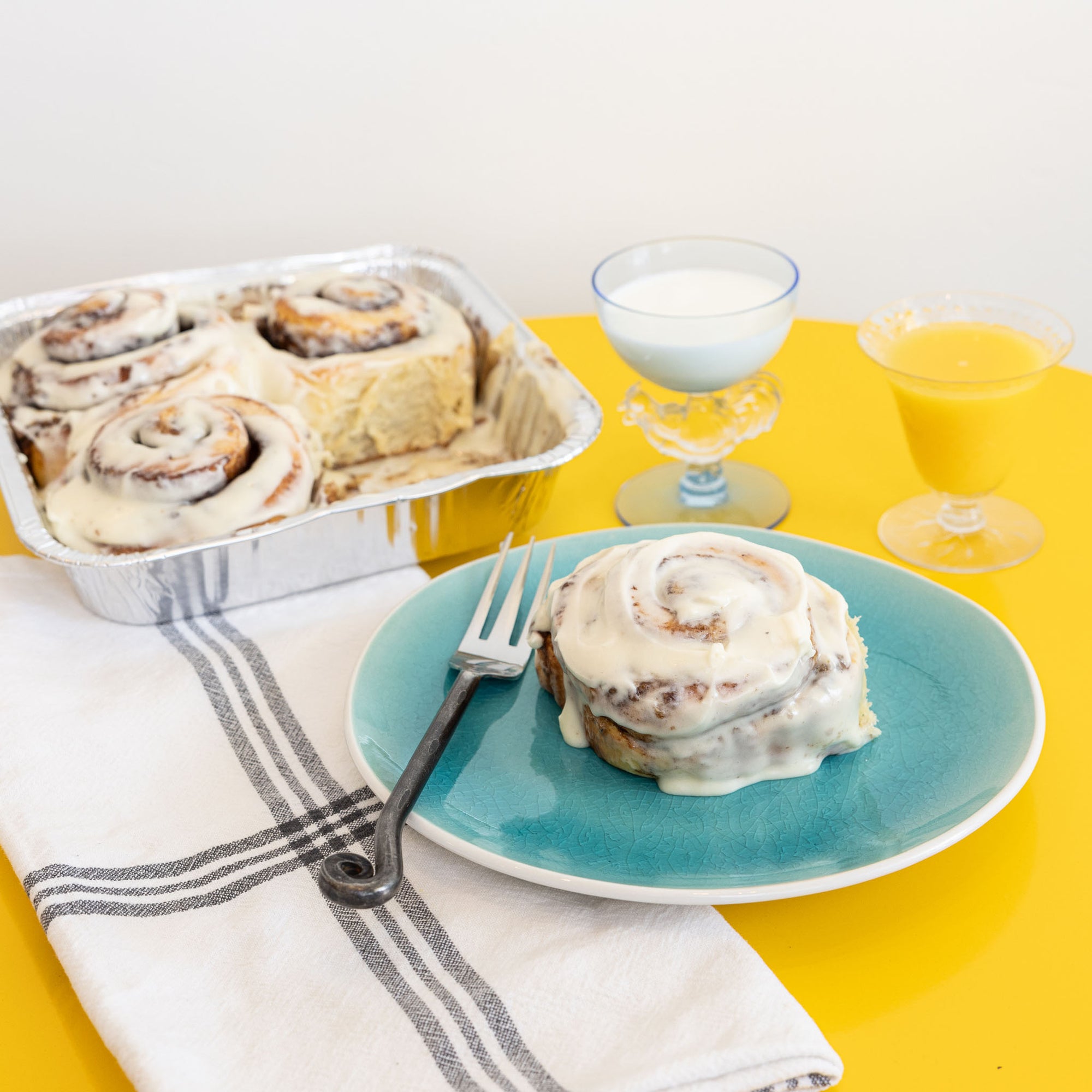 breakfast setting with cinnaon roll on a plate and a tray of cinnamon rolls in the background